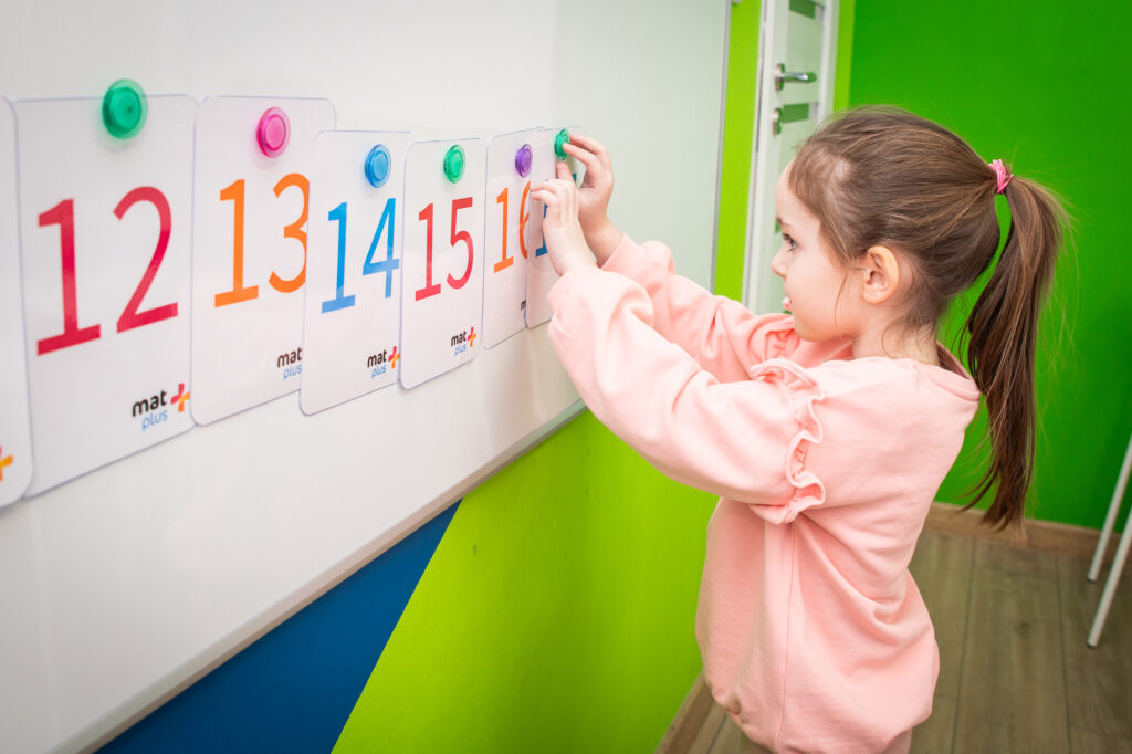 Dziewczynka przypina karty z liczbami do tablicy na zajęciach matematyki w MatPlus Wrocław